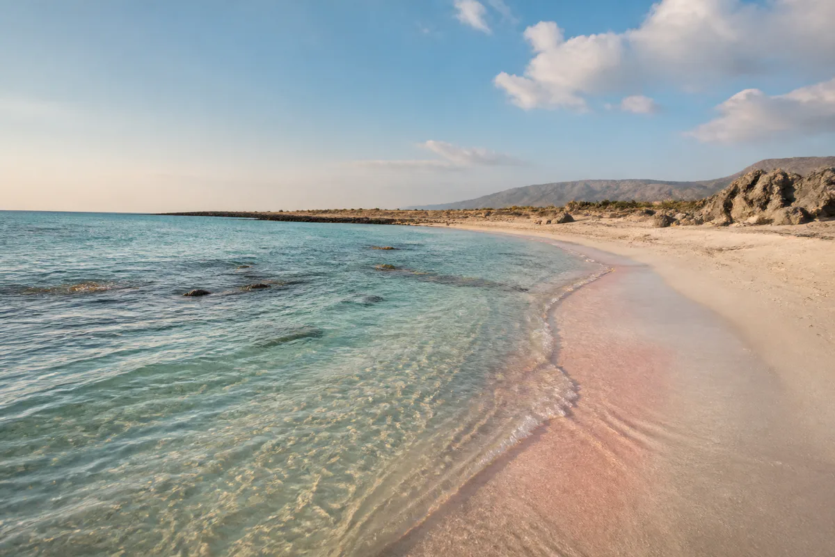 Shallow turquoise water meeting the pale pink shoreline at Elafonisi in south-west Crete