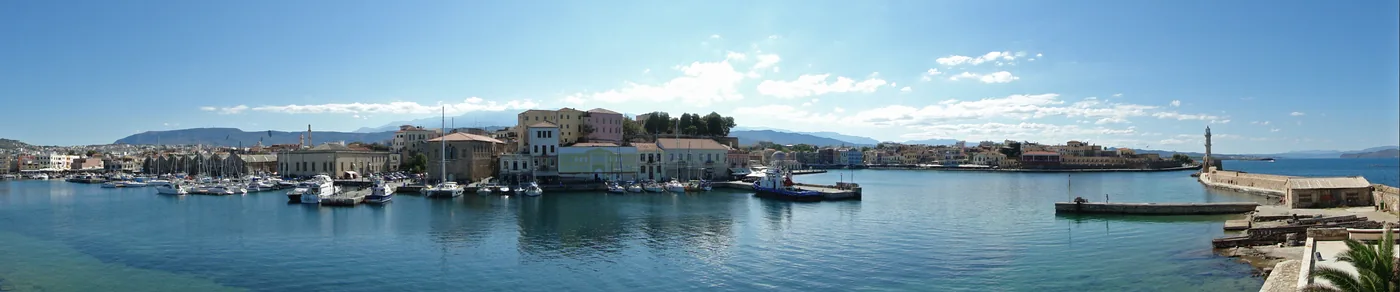 Panorama of Chania’s Venetian harbour: the waterfront, moored boats and the lighthouse at the end of the breakwater.