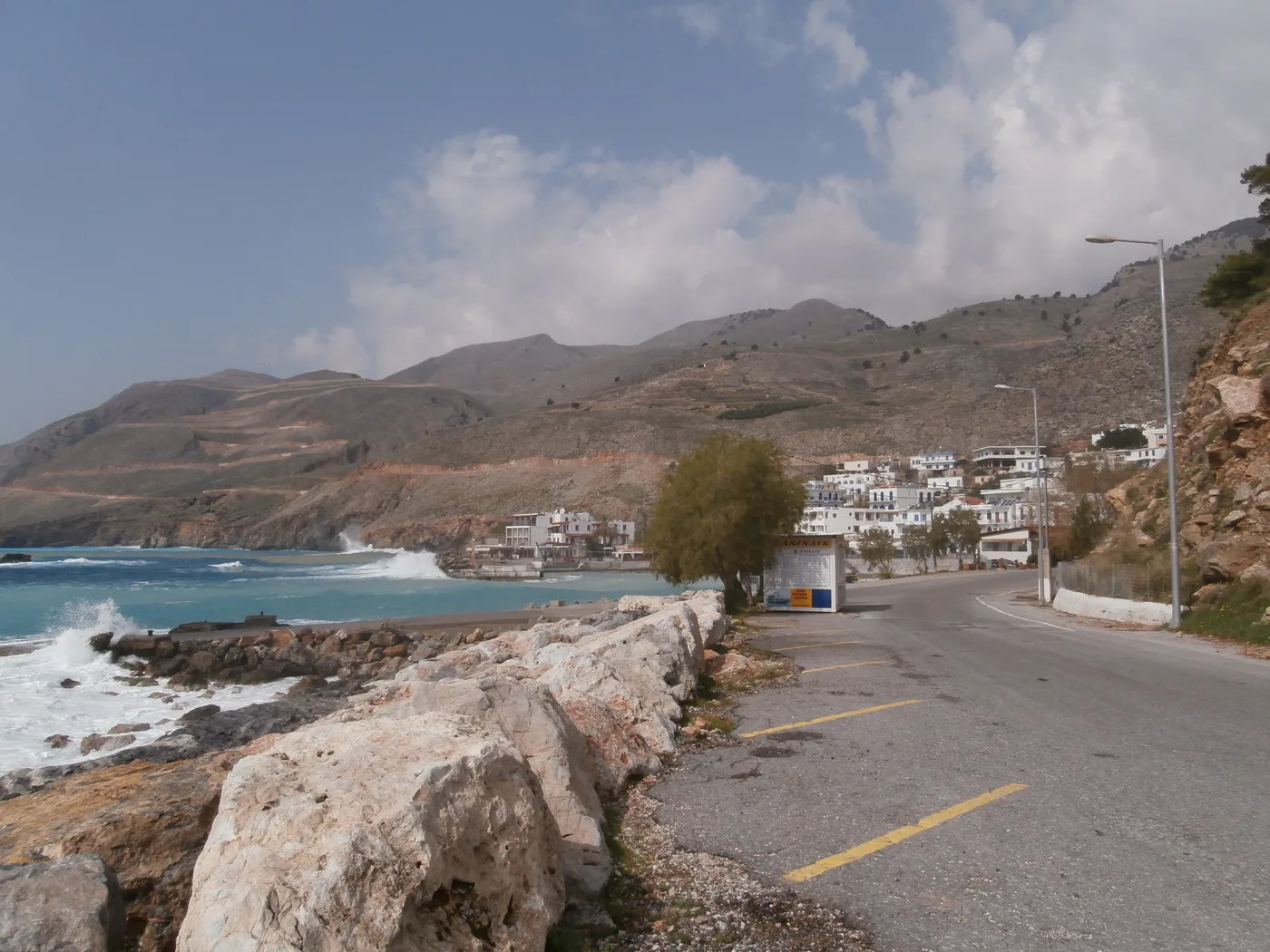 The road into Chora Sfakion along a rocky shore, with the white village on the hillside and mountains behind.
