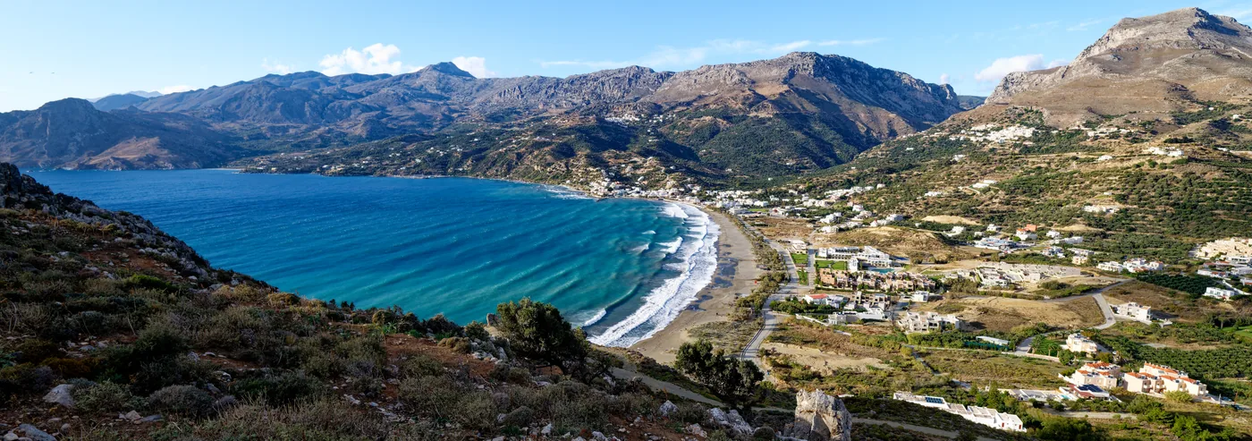 Plakias bay from the hill above the village: a long curved beach, the village along it and mountains behind.